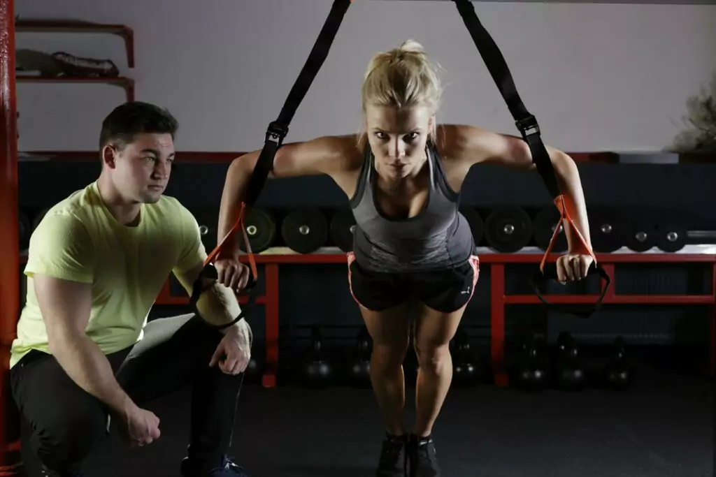 A woman performing strength training with a trainer in a gym setting, showcasing fitness and dedication.
